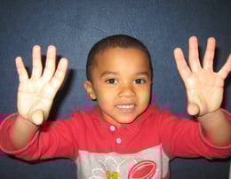 Kid wearing red and gray shirt with hands pointing up