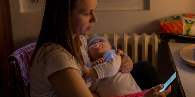young mother looking at her phone holding a sleeping baby
